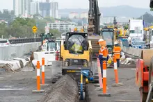Construction workers operating various machines and equipment on a busy roadwork site, ensuring safety and progress.